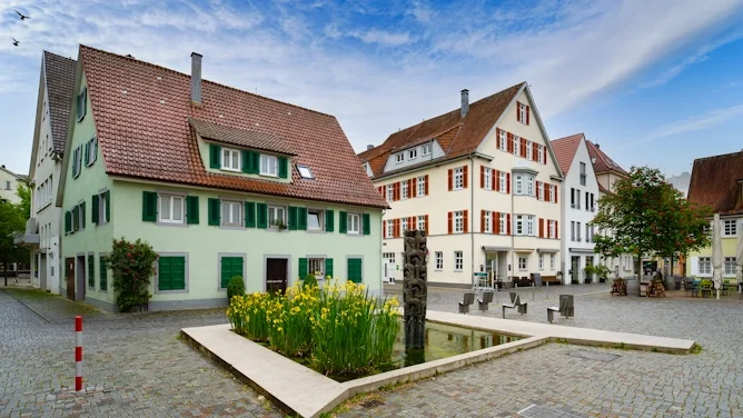 Blick auf einen historischen Platz in Göppingen mit hellen Gebäuden, roten Dächern, grünen Fensterläden, Brunnenanlage und gepflasterter Umgebung. Das Bild wird auf der Standortseite Göppingen von GARANT Immobilien verwendet und steht für den regionalen Immobilienmarkt, familienfreundliche Wohnlagen und Immobilienberatung in Göppingen, Uhingen, Eislingen, Süßen und Umgebung.