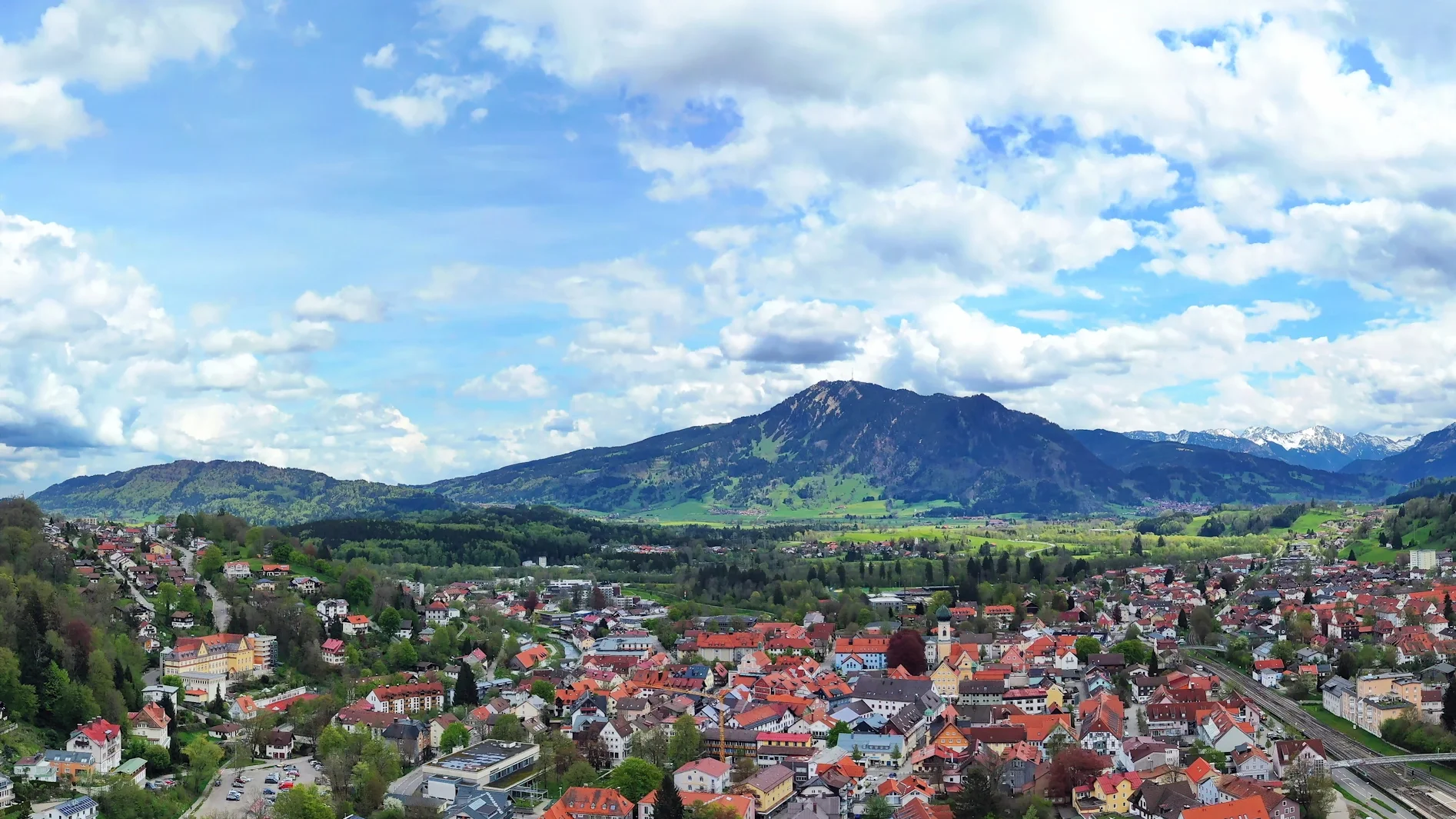 Luftaufnahme einer Stadt im Allgäu mit roten Dächern, grüner Landschaft und Bergen im Hintergrund. Das Bild wird als Header der Standortseite Allgäu von GARANT Immobilien verwendet und steht für regionale Immobilienberatung in Kaufbeuren, Kempten, Memmingen und dem gesamten Allgäu.