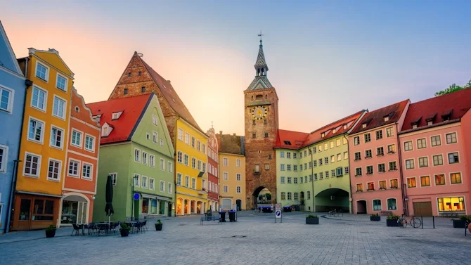 Blick auf den historischen Marktplatz in Landsberg am Lech mit bunten Fassaden, roten Dächern, Stadttor, Kirchturm und gepflastertem Platz. Das Bild wird auf der Standortseite Landsberg am Lech von GARANT Immobilien verwendet und steht für den regionalen Immobilienmarkt, historische Wohnlagen und Immobilienberatung in Landsberg am Lech, Kaufering, Igling, Pürgen, Finning und Umgebung.
