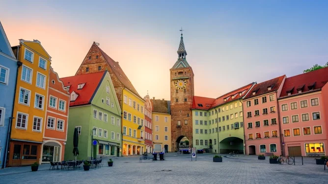 Blick auf den historischen Marktplatz in Landsberg am Lech mit bunten Fassaden, roten Dächern, Stadttor, Kirchturm und gepflastertem Platz. Das Bild wird auf der Standortseite Landsberg am Lech von GARANT Immobilien verwendet und steht für den regionalen Immobilienmarkt, historische Wohnlagen und Immobilienberatung in Landsberg am Lech, Kaufering, Igling, Pürgen, Finning und Umgebung.
