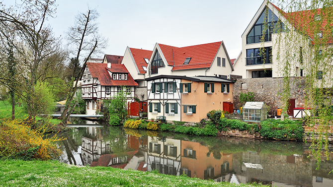 Blick auf Wohnhäuser im Rems-Murr-Kreis mit Fachwerkgebäuden, modernen Häusern, roten Dächern, viel Grün und Spiegelungen im Wasser. Das Bild wird auf der Standortseite Rems-Murr-Kreis von GARANT Immobilien verwendet und steht für den regionalen Immobilienmarkt, naturnahe Wohnlagen und Immobilienberatung in Waiblingen, Schorndorf, Backnang, Fellbach und Umgebung.
