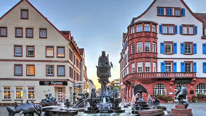 Blick auf eine historische Innenstadtansicht in Kaiserslautern mit Brunnen, klassischen Fassaden, roten Dächern und blau gestrichenen Fensterläden. Das Bild wird auf der Standortseite Kaiserslautern von GARANT Immobilien verwendet und steht für den regionalen Immobilienmarkt, attraktive Wohnlagen und Immobilienberatung in Kaiserslautern, Landstuhl, Otterberg, Enkenbach Alsenborn, Pirmasens und der Westpfalz.
