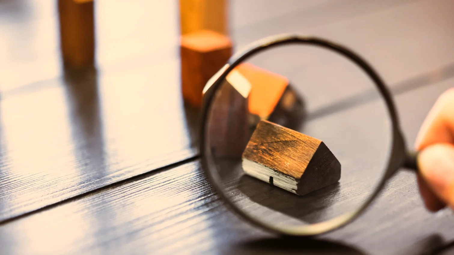 Eine Hand hält eine Lupe über ein Miniaturhaus auf einem Tisch. Das Bild wird als Header der Themenwelt-Seite von GARANT Immobilien verwendet und steht für Ratgeberthemen und Informationen rund um Immobilien, Gewerbeimmobilien, barrierefreies Wohnen, Immobilienrente, Tippgeber und Energieausweis.