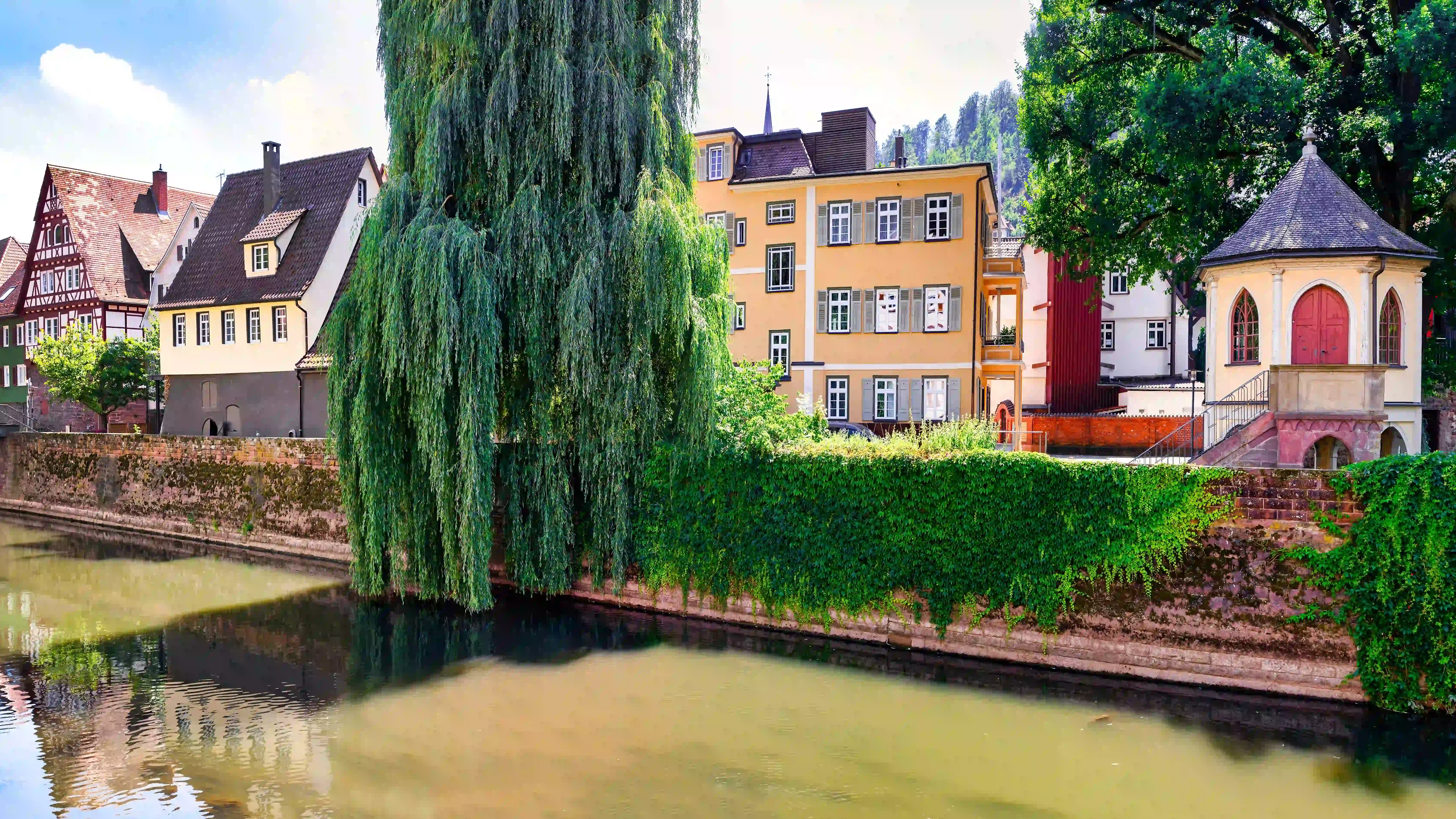 Blick auf eine historische Altstadt mit Fachwerkhäusern, begrüntem Ufer, Fluss und traditionellen Gebäuden. Das Bild wird als Header der Standortseite Calw und Freudenstadt von GARANT Immobilien verwendet und steht für regionale Immobilienberatung, lokale Marktkenntnis und persönliche Unterstützung rund um Immobilien in den Landkreisen Calw, Freudenstadt und Rottweil.