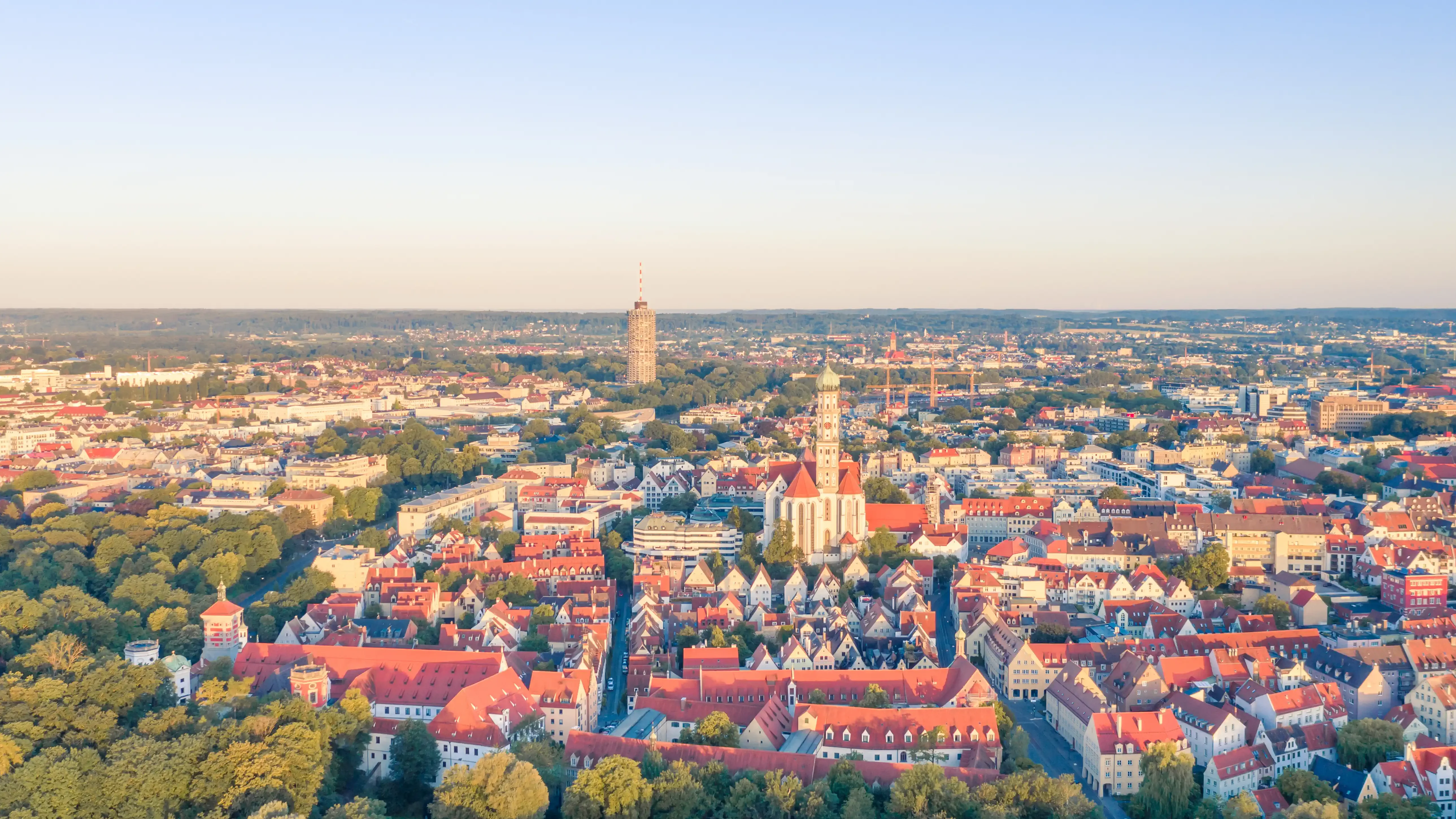 Luftaufnahme der Stadt Augsburg mit roten Dächern, historischen Gebäuden, Kirchtürmen und weitem Blick über die Region. Das Bild wird als Header der Standortseite Augsburg von GARANT Immobilien verwendet und steht für regionale Immobilienberatung, persönliche Betreuung und Immobilienvermittlung in Augsburg und Umgebung.