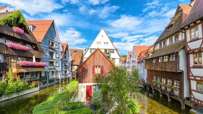 Blick auf eine historische Stadtansicht mit Fachwerkhäusern, Wasserlauf, grüner Umgebung und blauem Himmel. Das Bild wird auf der Standortseite Dornstadt von GARANT Immobilien verwendet und steht für den regionalen Immobilienmarkt, naturnahe Wohnlagen und Immobilienberatung in Dornstadt, Ulm, Neu-Ulm und Umgebung.