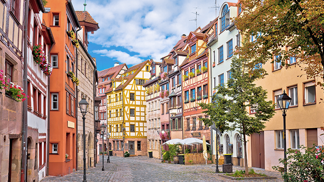 Blick in eine historische Altstadtgasse in Nürnberg mit Fachwerkhäusern, bunten Fassaden, gepflasterter Straße und klassischer Architektur. Das Bild wird auf der Standortseite Nürnberg von GARANT Immobilien verwendet und steht für den regionalen Immobilienmarkt, zentrumsnahe Wohnlagen und Immobilienberatung in Nürnberg, Fürth, Erlangen, Stein, Zirndorf und Schwabach.
