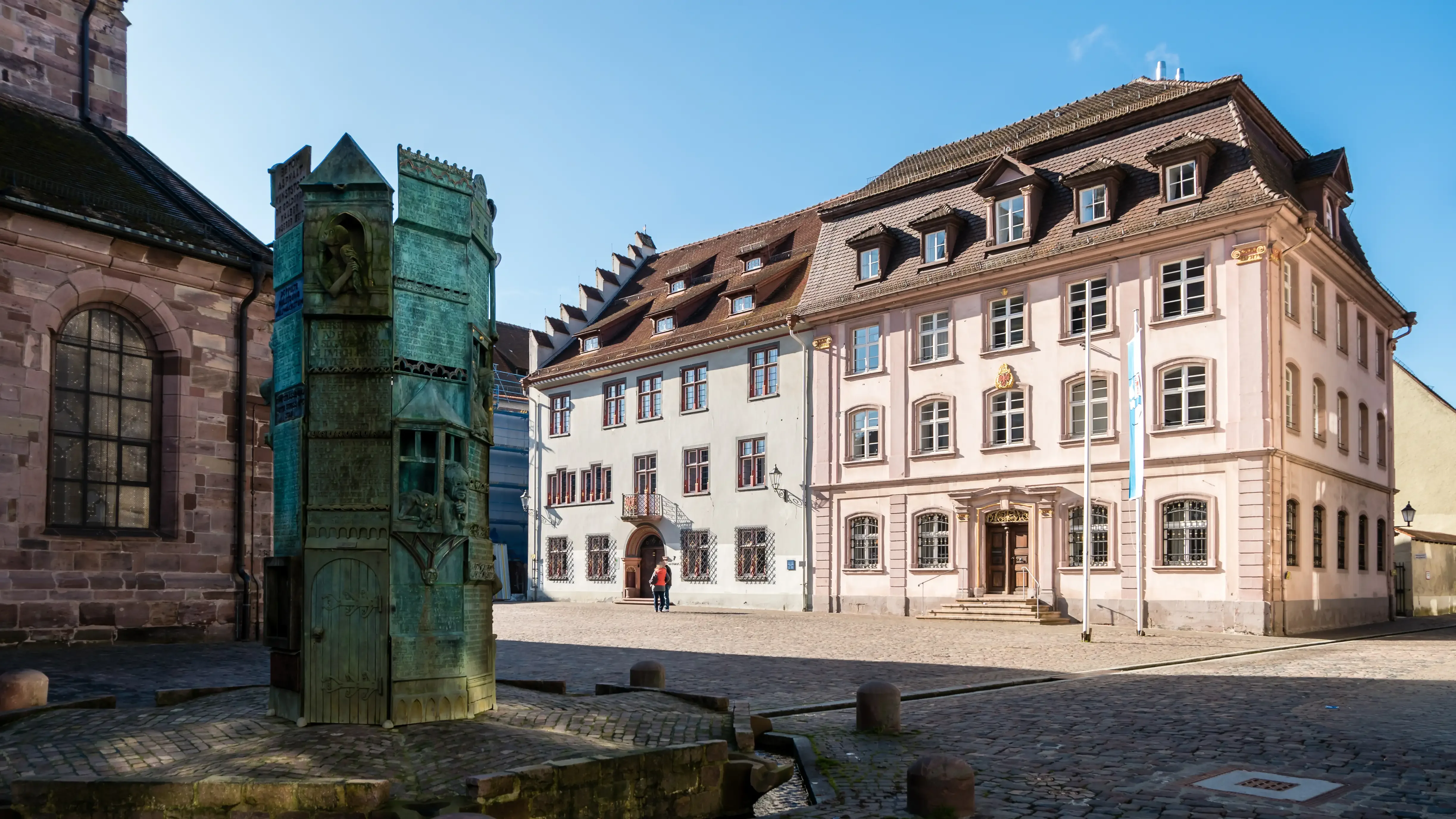 Blick auf ein historisches Gebäude in Villingen-Schwenningen mit gepflastertem Platz, Stadtbrunnen, klassischer Architektur und blauem Himmel. Das Bild wird auf der Standortseite Villingen-Schwenningen von GARANT Immobilien verwendet und steht für den regionalen Immobilienmarkt, historische Wohnlagen und Immobilienberatung in Villingen-Schwenningen, Schwarzwald-Baar-Kreis und Umgebung.