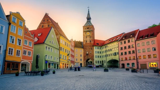 Blick auf den historischen Marktplatz in Landsberg am Lech mit bunten Fassaden, roten Dächern, Stadttor, Kirchturm und gepflastertem Platz. Das Bild wird auf der Standortseite Landsberg am Lech von GARANT Immobilien verwendet und steht für den regionalen Immobilienmarkt, historische Wohnlagen und Immobilienberatung in Landsberg am Lech, Kaufering, Igling, Pürgen, Finning und Umgebung.
