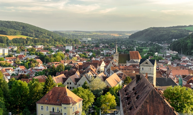 Blick über Hof mit historischen Gebäuden, roten Dächern, Kirchturm und grüner Hügellandschaft im Hintergrund. Das Bild wird auf der Standortseite Hof von GARANT Immobilien verwendet und steht für den regionalen Immobilienmarkt, naturnahe Wohnlagen und Immobilienberatung in Hof, Bayreuth und den umliegenden Landkreisen in Oberfranken.