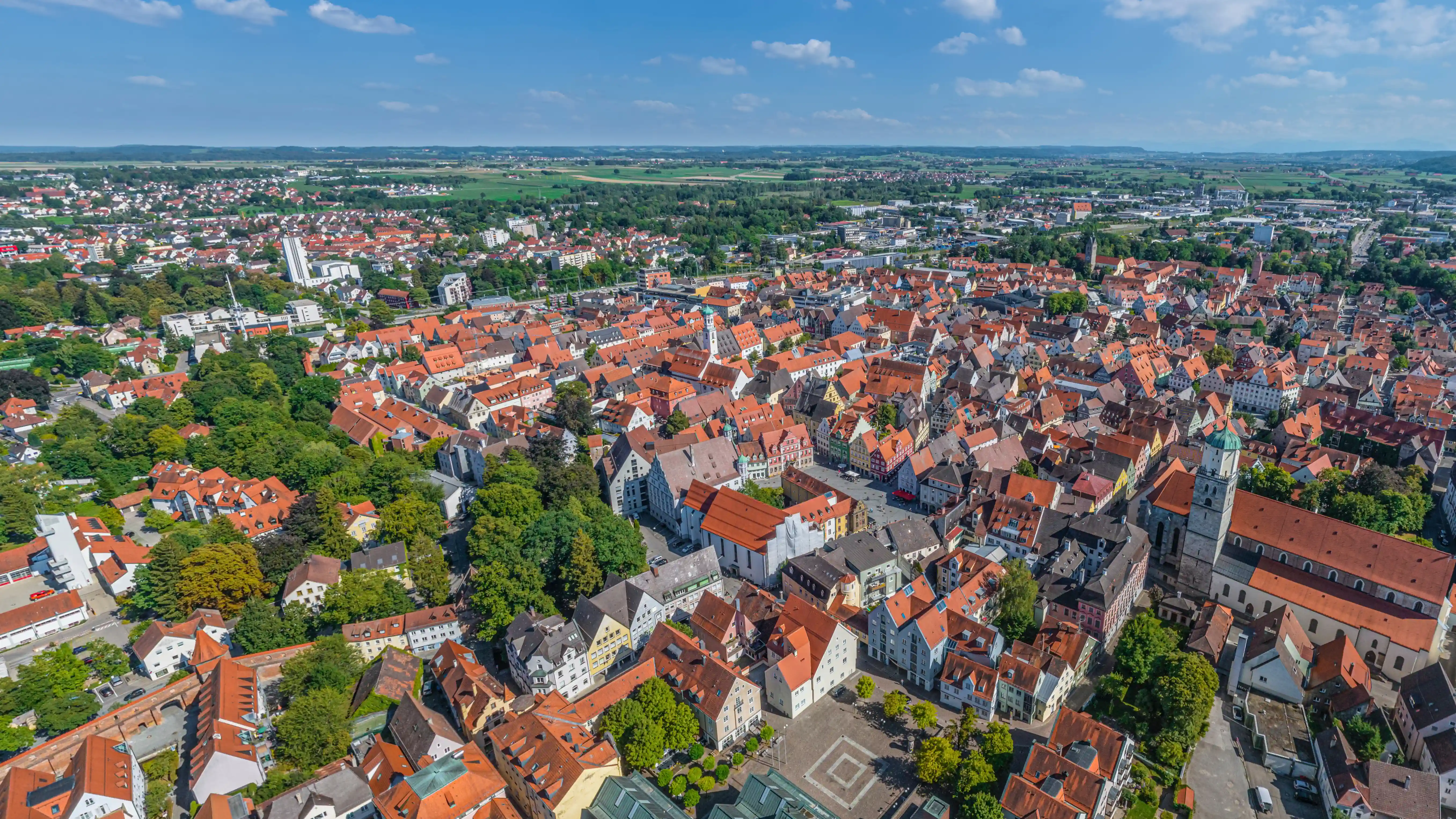 Luftaufnahme von Memmingen mit Blick über die historischen Dächer der Altstadt, Kirchtürme und die umliegende grüne Landschaft unter blauem Himmel.