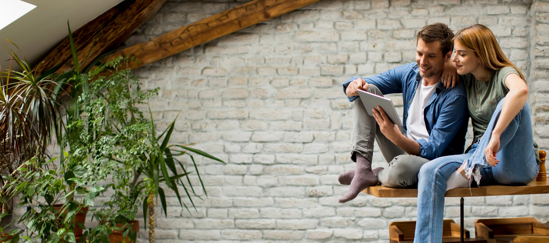 Ein Paar sitzt gemeinsam in einem modernen Wohnraum und schaut auf ein Tablet. Das Bild wird als Header der Referenzen-Seite von GARANT Immobilien verwendet und steht für erfolgreich vermittelte Immobilien sowie die digitale Übersicht über Referenzobjekte.